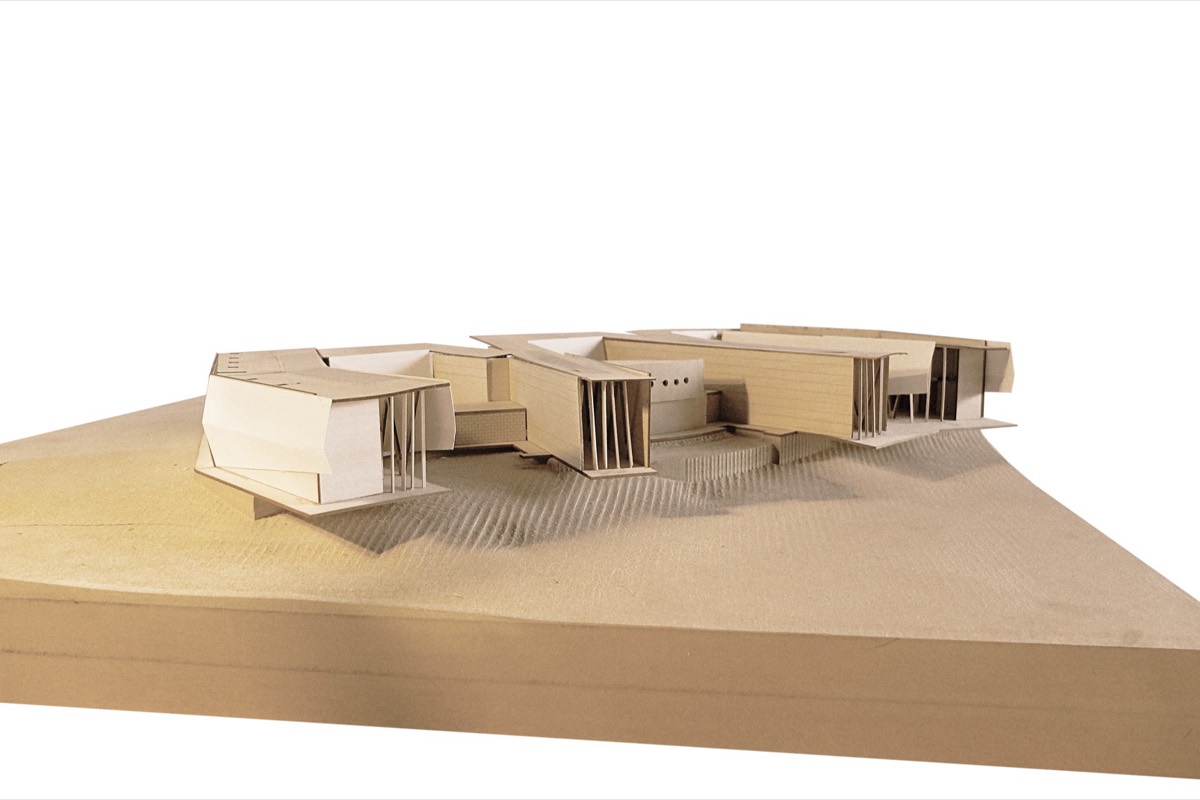 A laser-cut wood study model of a low building on a shaped topographic base, photographed against white.